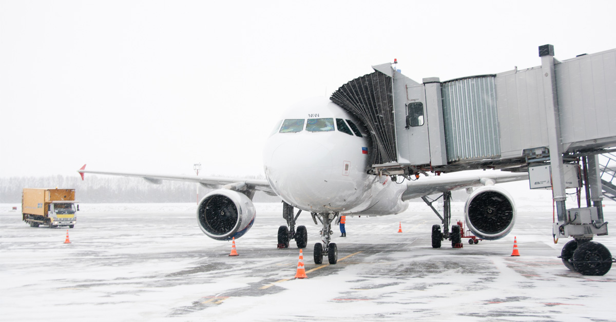 Airplane on snowy tarmac with bridge extended.